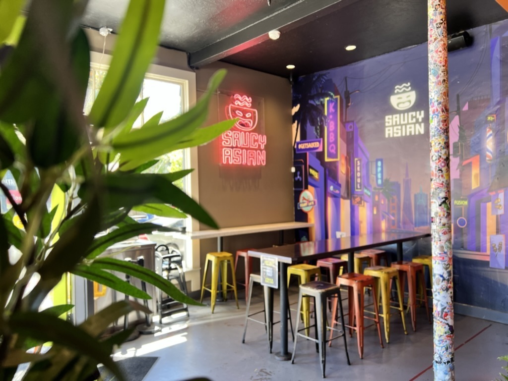 The interior of Saucy Asian, with neon stools and a mural on the wall